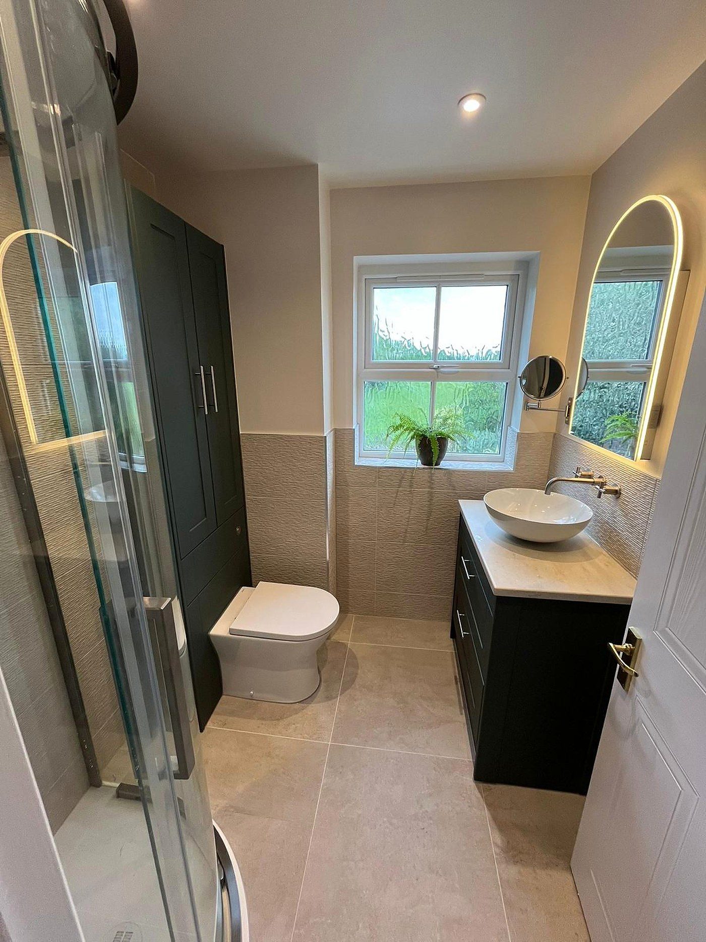 A modern fitted bathroom with a walk in shower, dark vanity unit and a brass tap