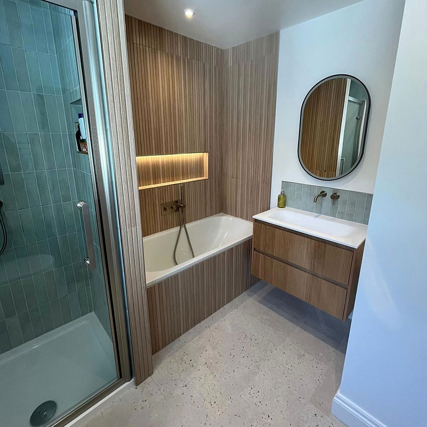 A finished bathroom with a glazed shower enclosure, a panelled bath and a wall hung timber vanity unit