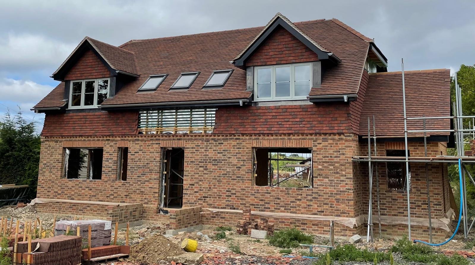 A large brick and clay tile house under construction with scaffold, new dormer windows and open window reveals