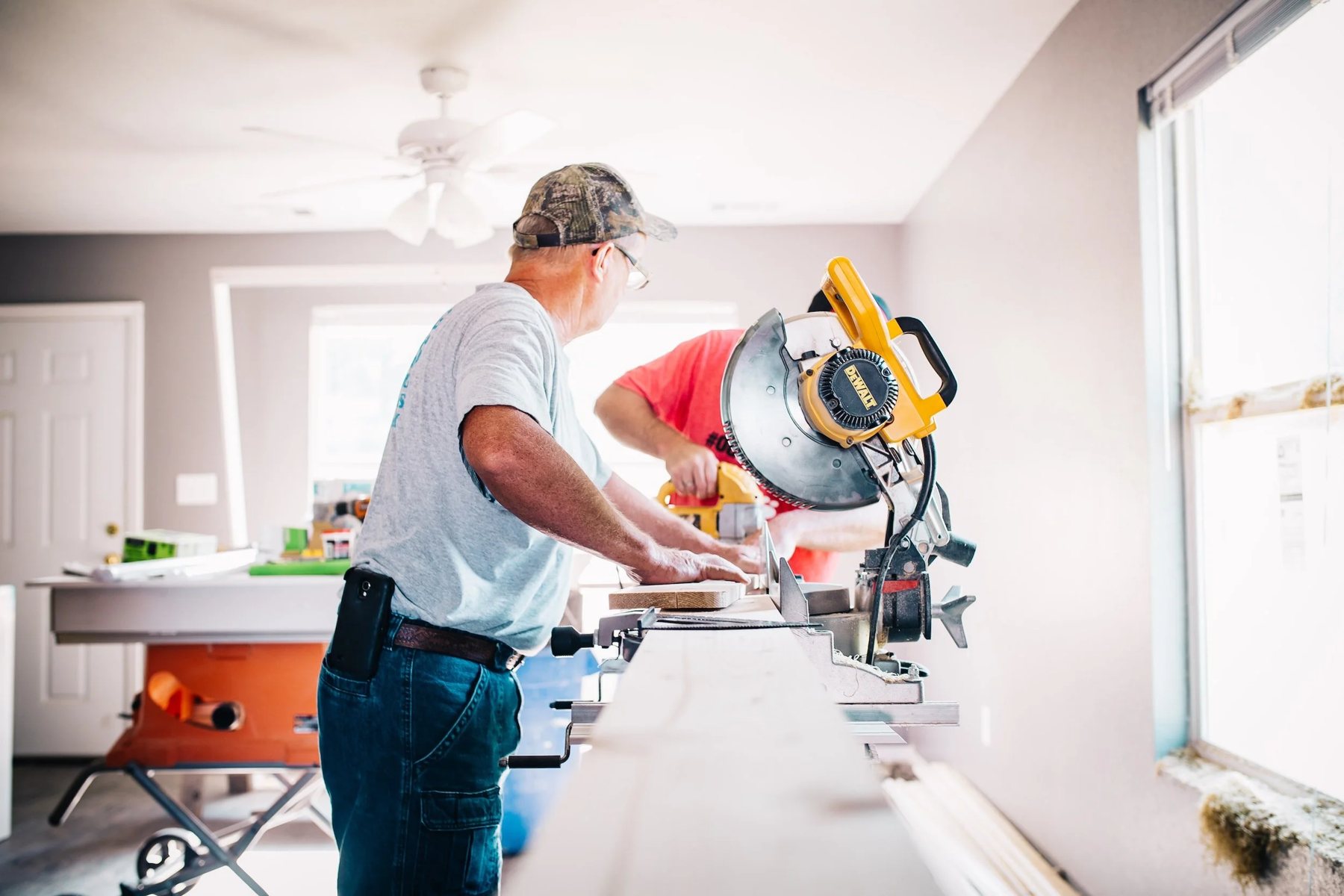 A carpenter cutting timber on a mitre saw during a fit out, with a second joiner working at the bench behind him