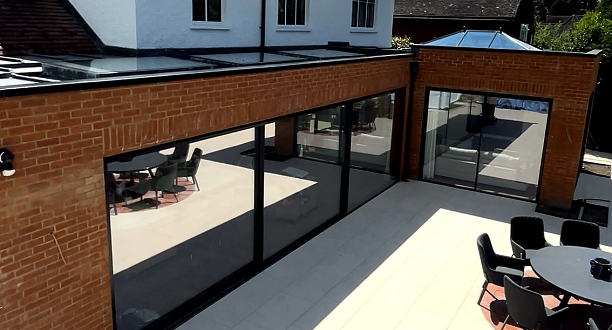 A finished brick wraparound extension by I.C Developments with anthracite sliding glazing, a roof lantern and a large paved patio