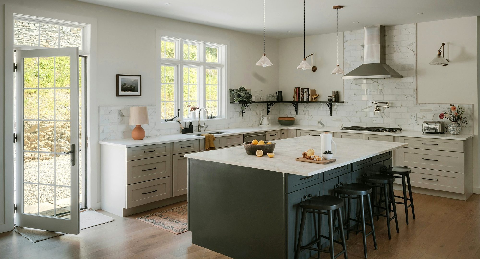 A bright shaker kitchen with a marble worktop, charcoal island, bar stools and a glazed door open to the garden