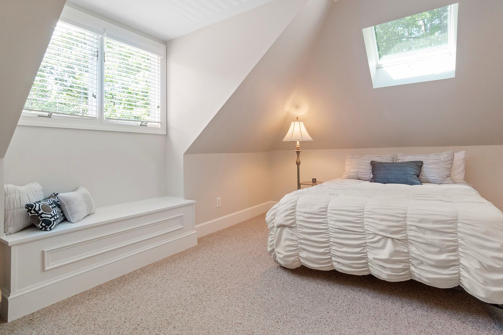 A finished loft bedroom with a bright neutral finish and a window seat under the eaves