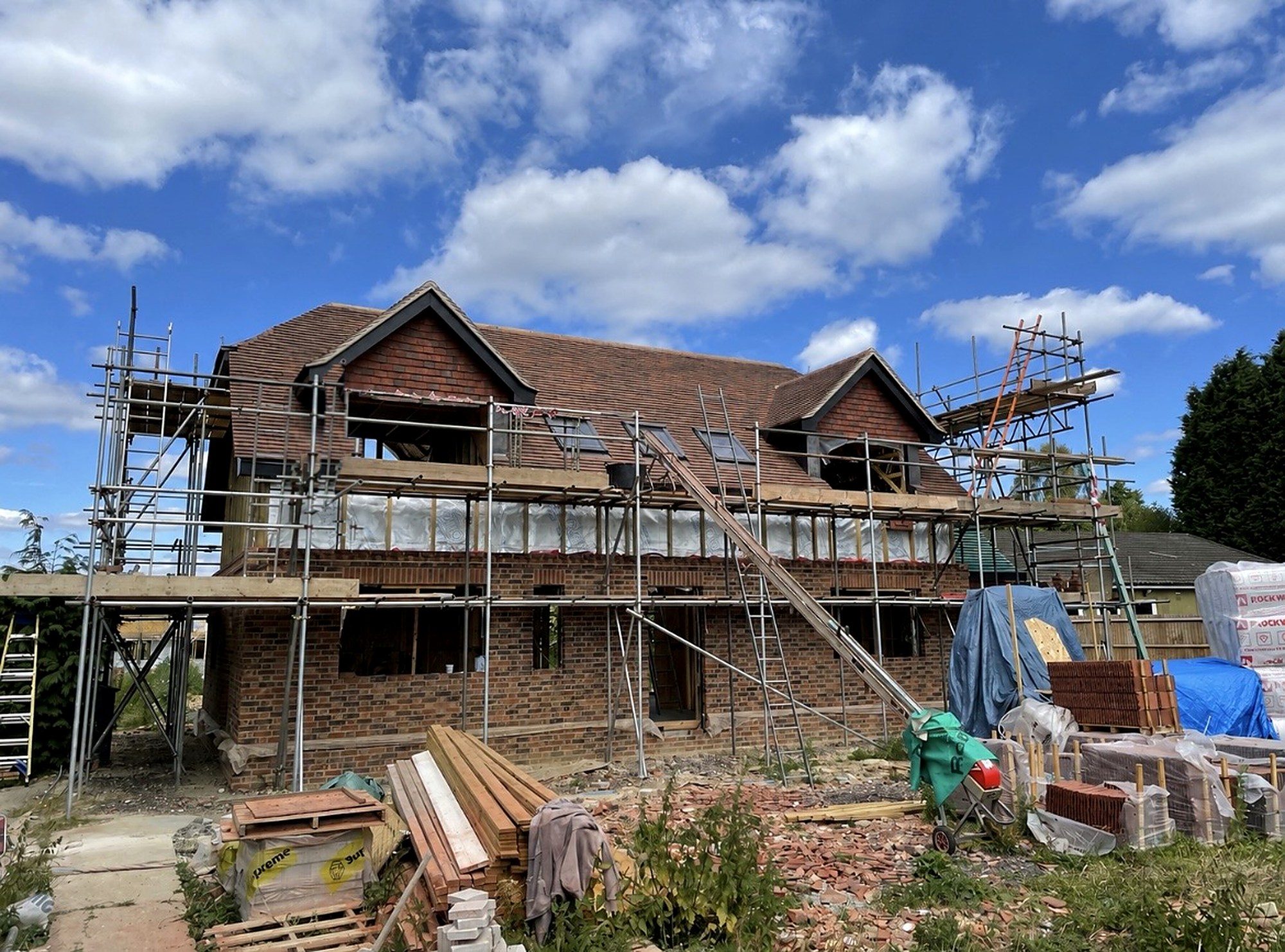 A brick and tile new build home under scaffold, nearing completion on an I.C Developments site in Surrey
