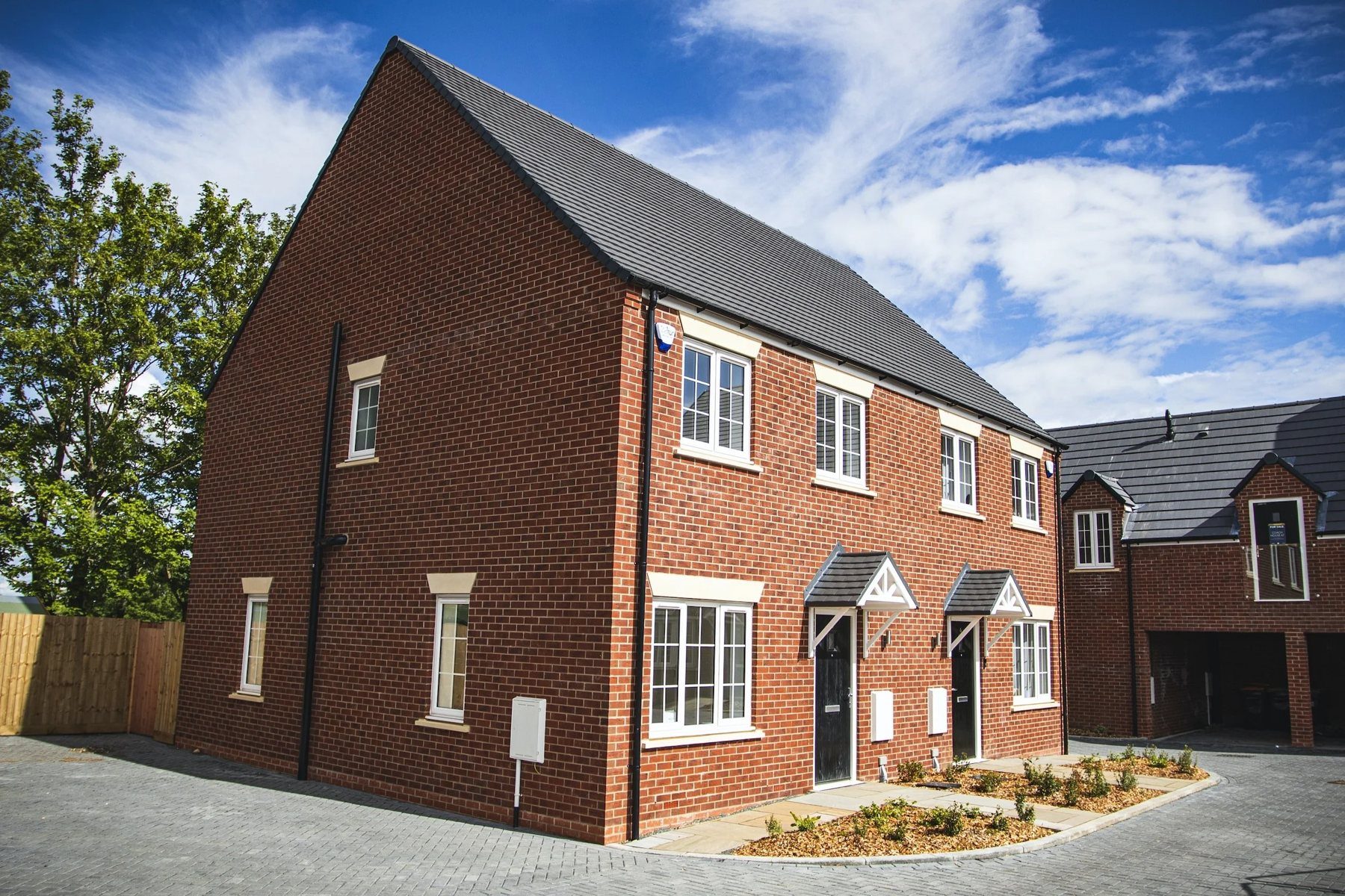 A pair of completed brick new-build homes under a blue sky